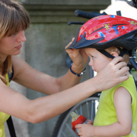Eine Frau befestigt den Fahrradhelm eines Kindes Eine Frau befestigt den Fahrradhelm eines Kindes