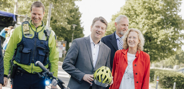 Innenstaatssekretär Sandro Kirchner mit Sabine Roidl, Vizepräsidentin der Landesverkehrswacht Bayern und einem Polizisten hinter einem blauen Fahrrad stehend