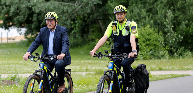 Aktionsmonat Fahrradsicherheit - © ©BayStMI links Innenminister Joachim Herrmann und ein Polizist auf einem Fahrrad fahrend mit Fahrradhelm auf Fahrradstraße